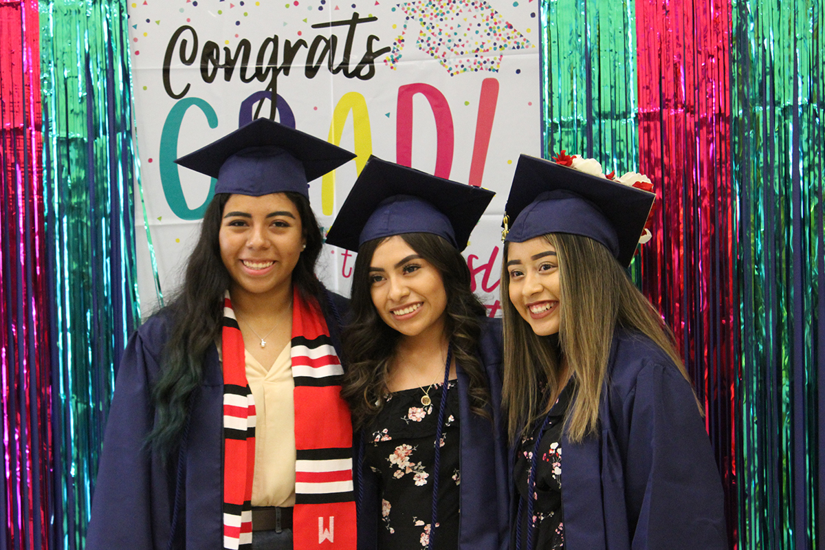 Three migrant students at graduation wearing caps and gowns