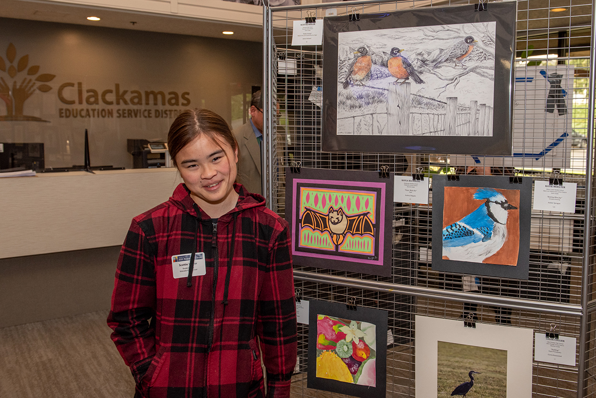 Teenage student smiling in front of her displayed drawing of robins.