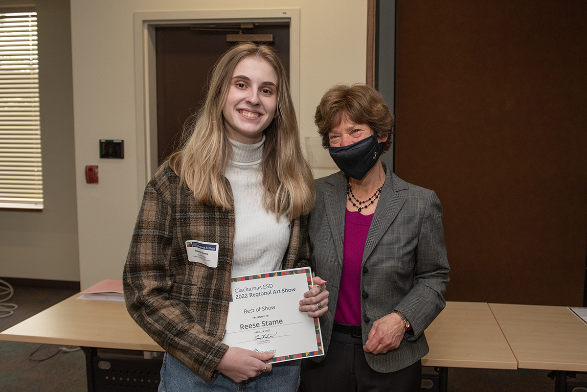 Best in show winner Reese Stame holding her award certificate and smiling with CESD Board Member Linda Brown