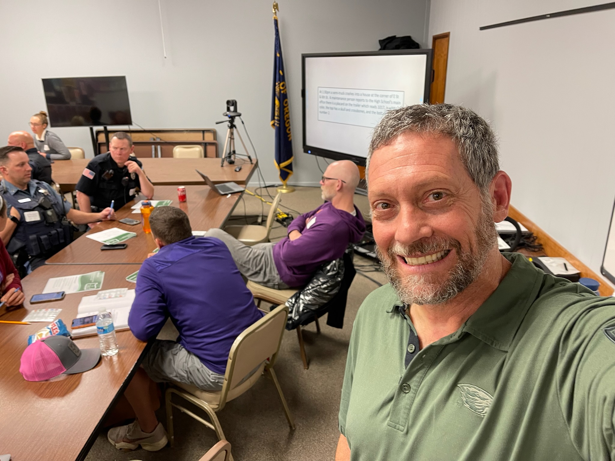 A smiling selfie of Dan Kraus, Clackamas ESD’s emergency operations/school safety specialist, leading a training session in a conference room with uniformed officers in attendance