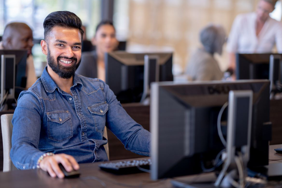Man smiling at desktop computer while taking a test in a computer lab with other adults