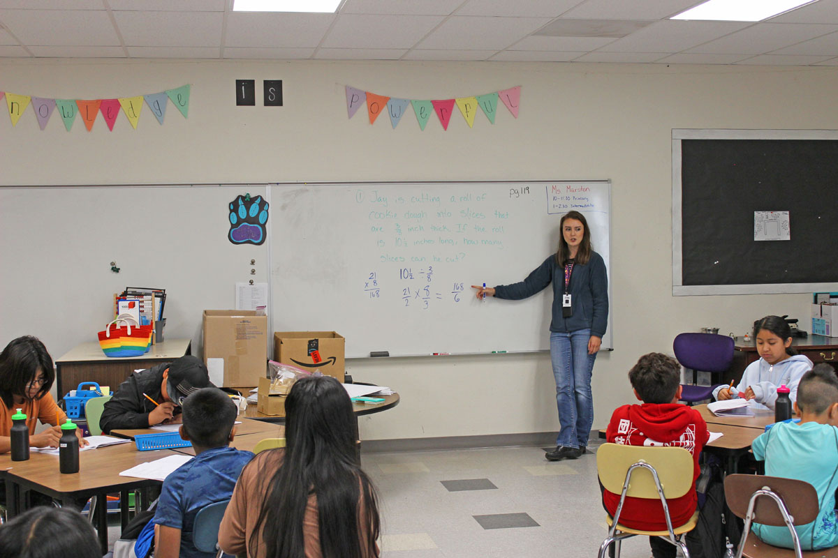 Migrant education program teacher points to math equation on a whiteboard in front of a classroom of focused students
