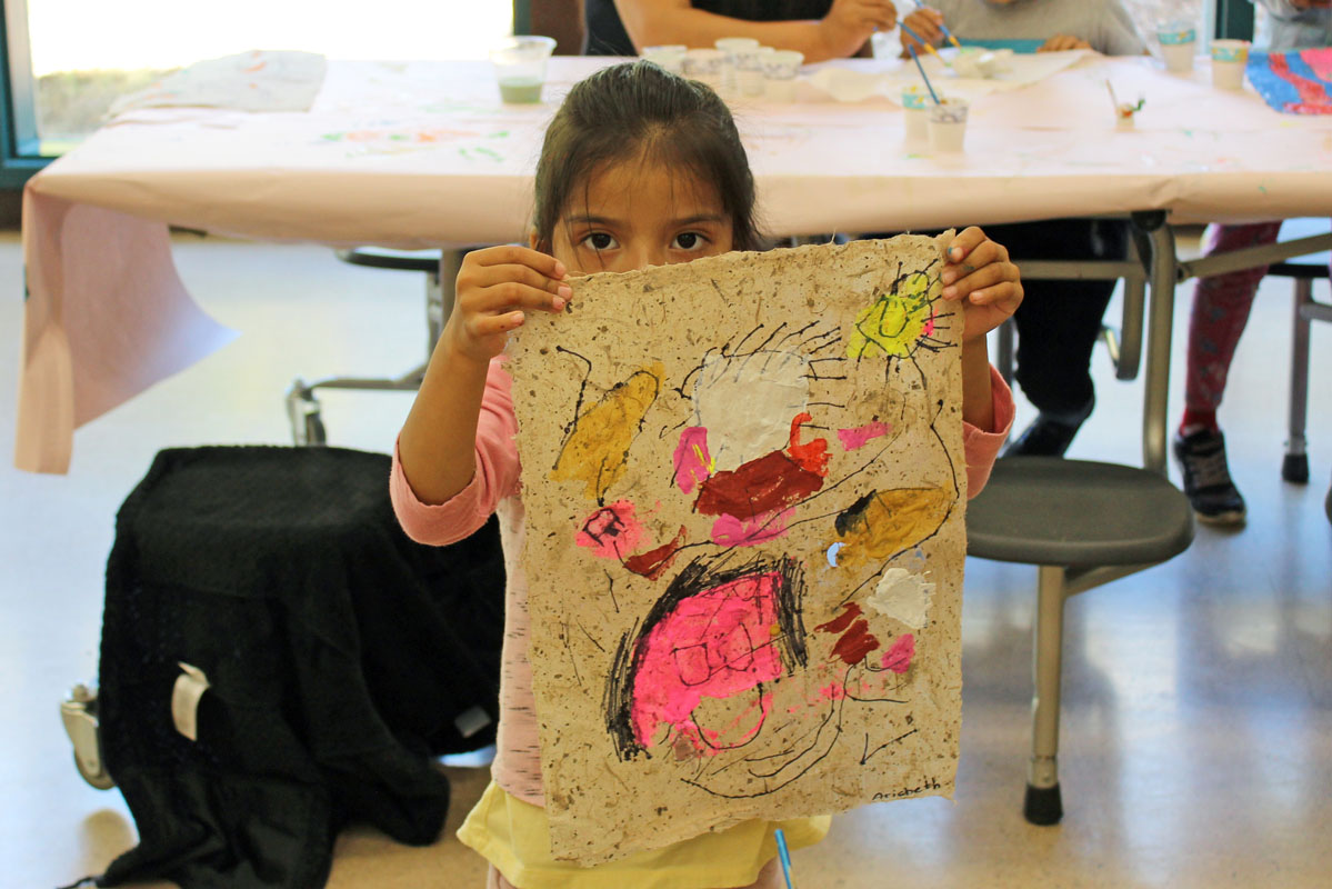Migrant student holds up her colorful bark painting