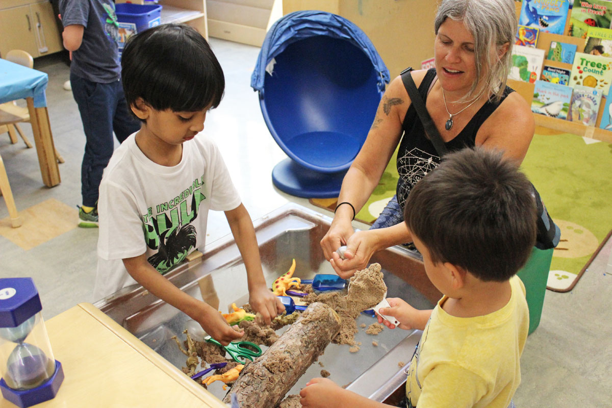 Two preschool children play with kinetic sand with a staff member