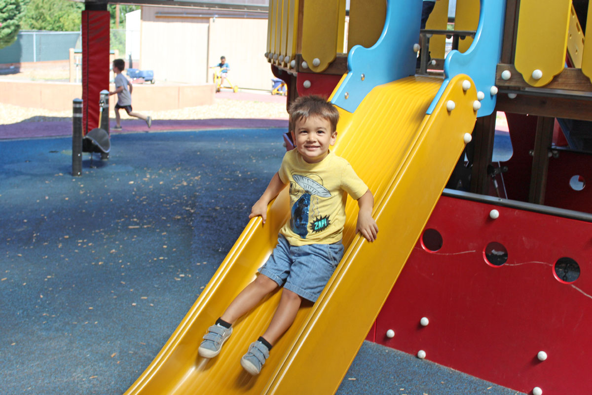Preschool student slides down a slide in the school playground
