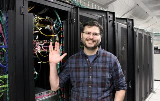 John Gates smiling and holding up the Vulcan salute in the server room