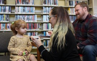 A parent smiles as he watches a Clackamas ESD staff member test his daughter's hearing at a free screening event at Gladstone Public Library
